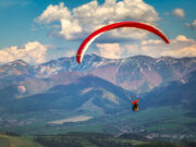 Paraglidingový pilot vo vzduchu, bezpečne lietajúci nad horskou krajinou.