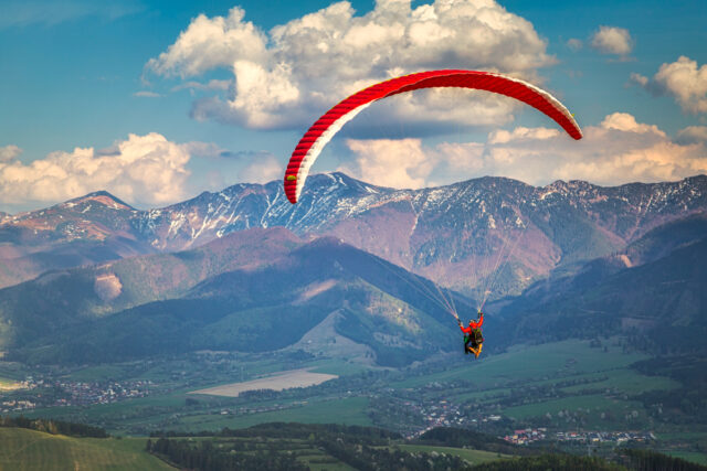 Paraglidingový pilot vo vzduchu, bezpečne lietajúci nad horskou krajinou.